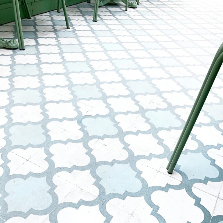Geometric quatrefoil pattern tiles with green metal furniture legs in a modern setting.